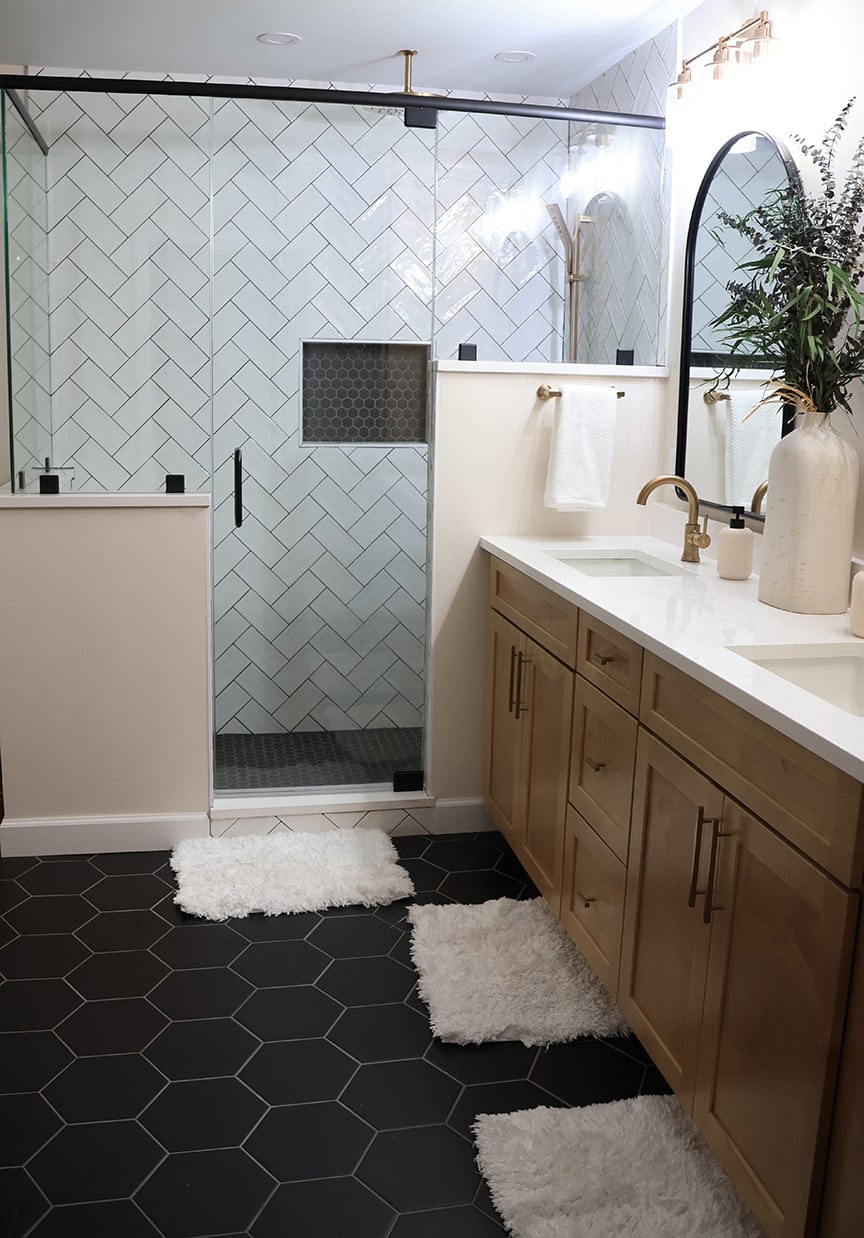 primary bath with natural wood cabinetry, black hexagonal floor tile and herringbone white shower tile