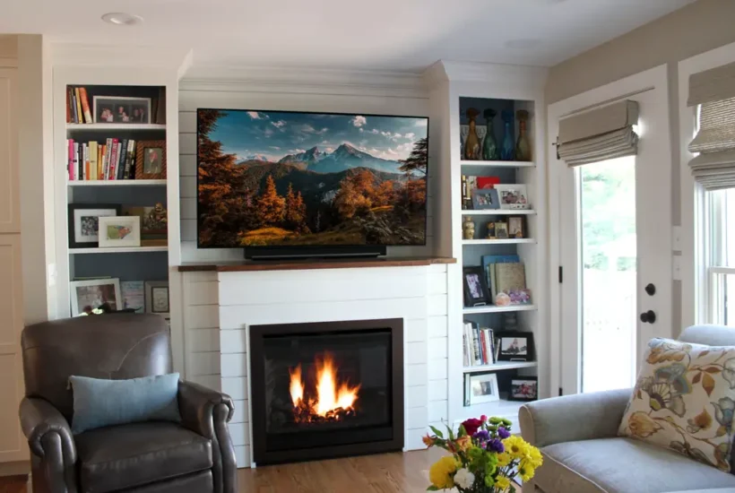 A home living space with seating, book shelves, a fireplace, and tv on hearth, by Agape Construction.