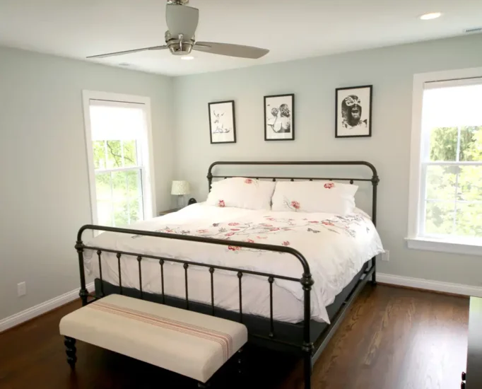 A metal-bedframe with light-colored bedding and dark, wooden floors in a primary bedroom.