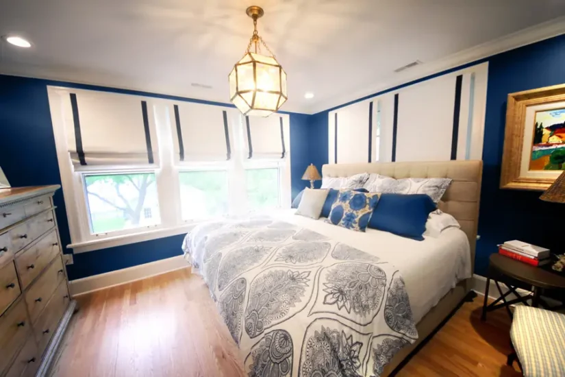 A primary blue bedroom with warm accents and matching bedspread. By Agape Construction.