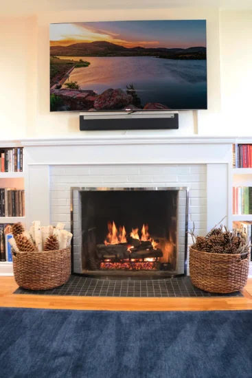A white brick and wood fireplace under a wall-mounted tv, featuring integrated shelving, by Agape Construction.