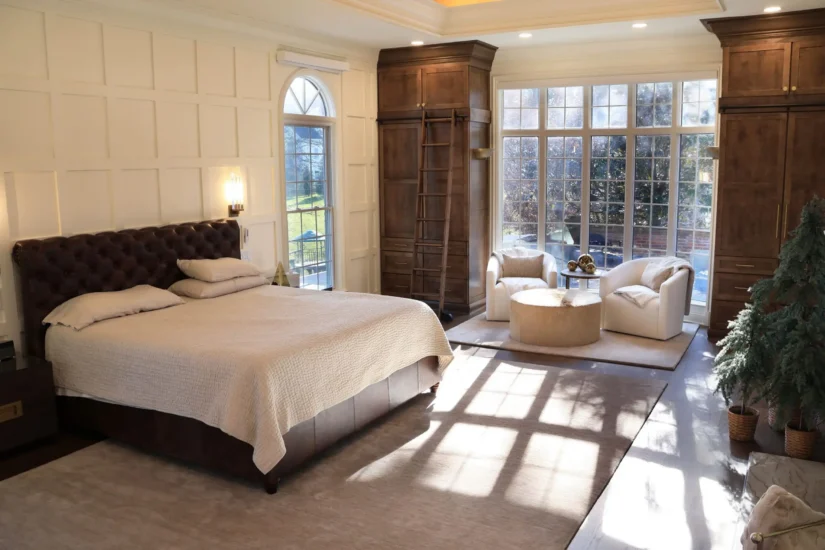 A primary bedroom featuring deep, wooden accents and ample natural light. By Agape Construction.